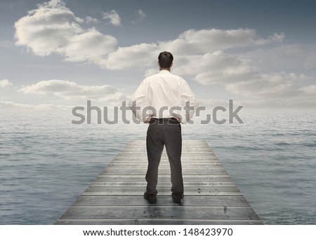 Businessman standing on a bridge with hands on hips and looking at the sea