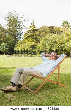 Happy mature man resting in sun lounger with hands behind his head in bedroom