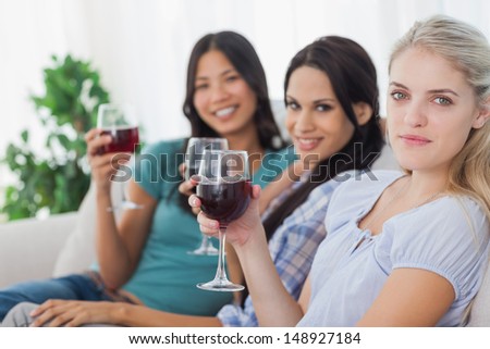 Cheerful friends having red wine together looking at camera at home on couch