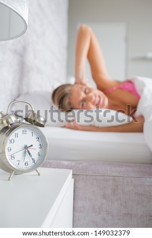 Irritated blonde covering her ears from the alarm clock noise at home in bedroom