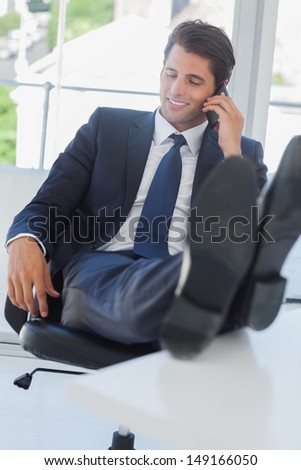 Businessman on the phone in his office relaxing with his feet on his desk