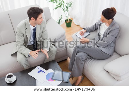 Businessman talking while colleague is taking notes sitting on sofa at office