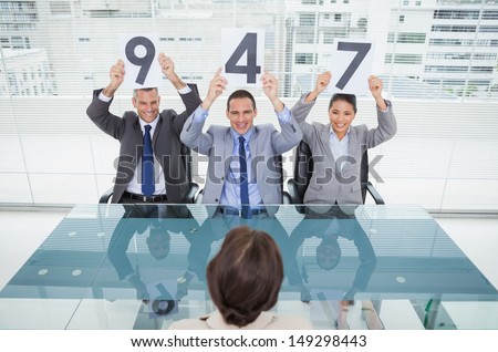 Smiling interview panel in bright office holding signs above their head giving marks to their applicant