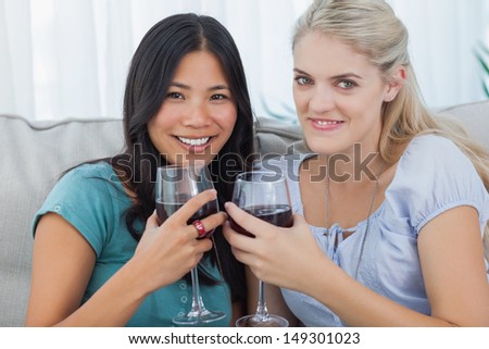 Smiling friends having red wine together looking at camera at home on couch
