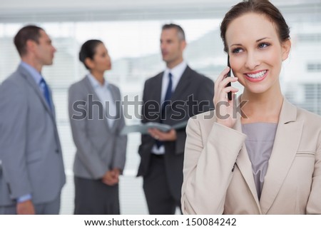 Smiling businesswoman in bright office calling while colleagues talking together