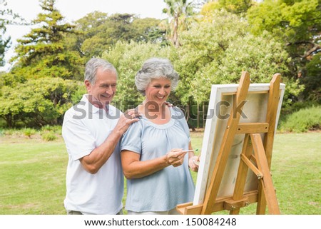 Cheerful retired woman painting on canvas with husband in the park on sunny day