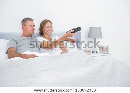 Cheerful couple watching tv in bed at home in bedroom