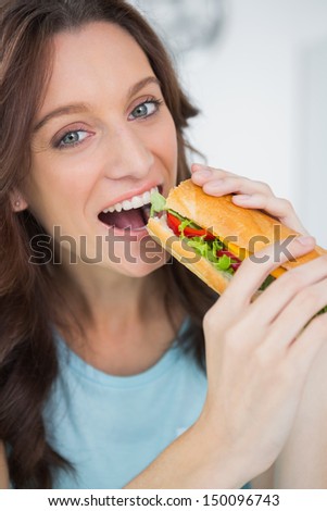 Cute brunette eating sandwich in her kitchen