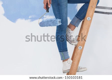 Woman holding paint roller on ladder against half painted wall