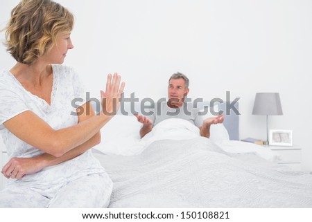 Annoyed woman looking at husband gesturing during a fight in bedroom at home