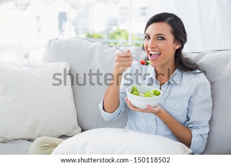 Cheerful woman relaxing on the sofa eating salad in her living room