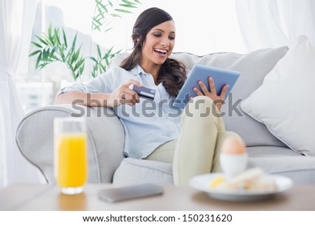 Laughing brunette buying online while having breakfast in her living room