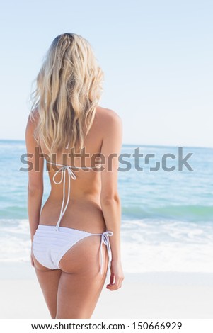 Beautiful blonde in white bikini looking at the sea at the beach