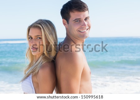 Young happy couple standing back to back at the beach
