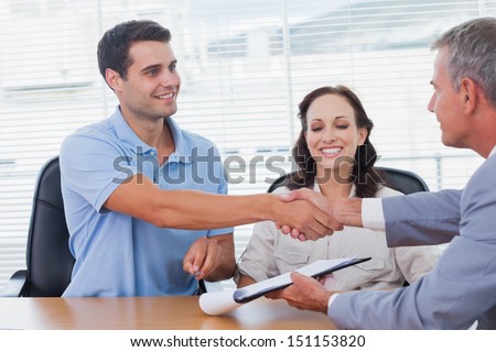 Handsome man with his wife shaking hands with estate agent  in bright office