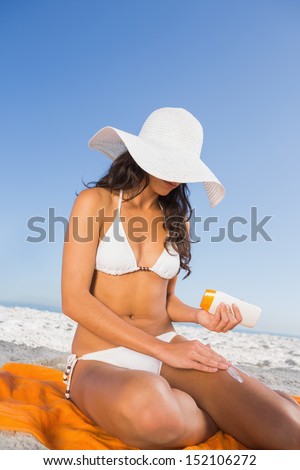 Sexy woman on the beach applying sun cream while sitting on her towel