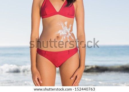 Slim woman body with sun cream on belly posing on a beach