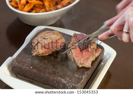 Steak sizzling on hot stone plate being sliced served in classy restaurant