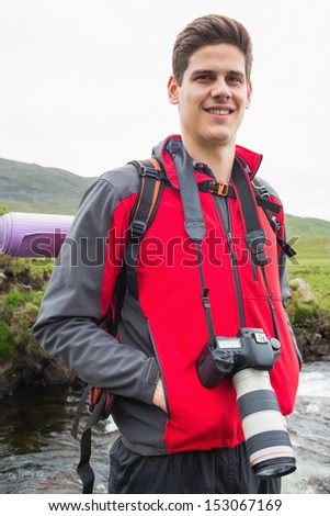 Happy man on a hike with a camera around his neck smiling at camera in the countryside