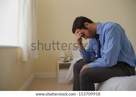 Mournful man sitting head in hands on his bed in a bedroom at home