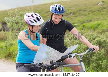 Couple on mountain bikes reading map on a trail in countryside