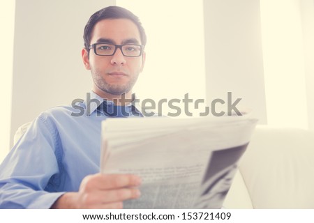Frowning man with glasses looking at camera and holding a newspaper