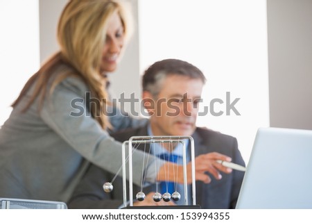 A businesswoman pointing something to a businessman with a newtons cradle in the foreground