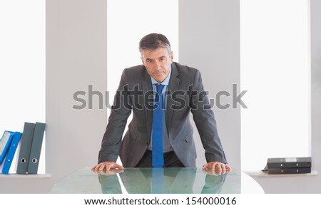 Frowning mature businessman standing firmly in front of a desk at office