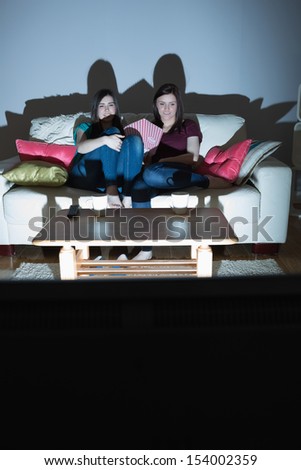 Two happy friends on the couch watching tv together in the dark at home in the living room