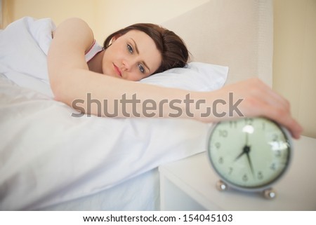 Sleepy brunette turning off her alarm clock in her bedroom