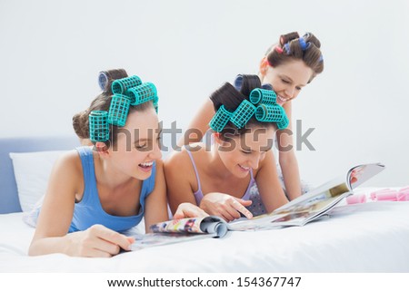 Girls wearing pajamas and hair rollers sitting in bed with magazines at sleepover