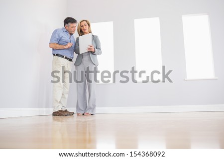 Concentrated blonde realtor showing an empty room and some documents to a potential attentive mature buyer