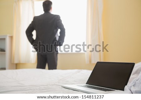 Businessman standing back hands in the pockets in front of the window in a bedroom