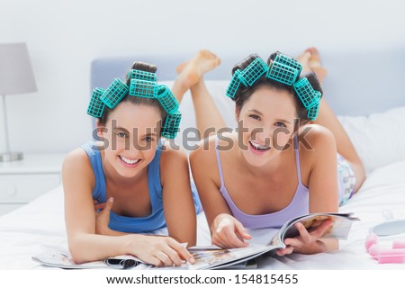 Girls in hair rollers holding magazines and smiling at camera at sleepover