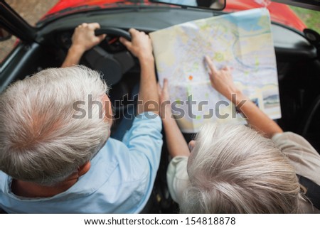 Overhead view of mature couple on holidays reading map in their classy convertible