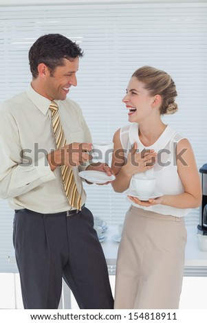 Stylish workmates laughing while having coffee together in break room