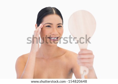 Natural dark haired model holding mirror touching her temple on white background