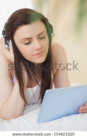 Relaxed girl listening to music with a headset and using a tablet pc lying on a bed in a bedroom