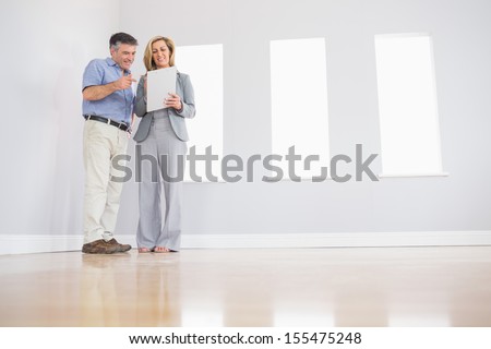 Cheerful blonde realtor showing an empty room and some documents to a potential attentive mature buyer