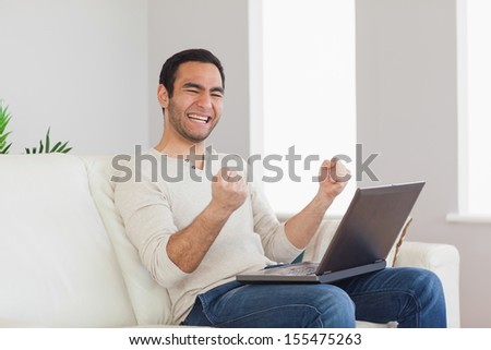 Successful casual man cheering while sitting in bright living room