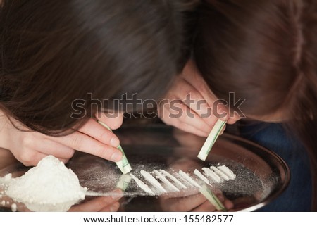 Two girls snorting an illegal white powder with dollar bills off a mirror