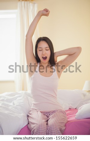 Young asian woman yawning and stretching in the morning in bedroom at home