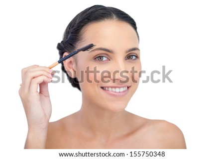 Smiling young brunette using eyebrow brush on white background