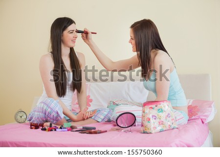 Smiling girl giving her friend a makeover at sleepover in bedroom at home