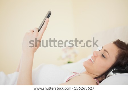Smiling girl listening music on her smartphone lying on bed in a bedroom