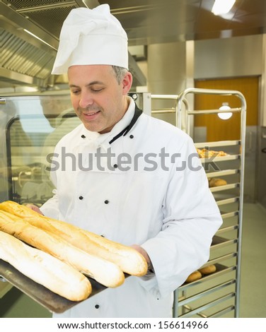 Mature head chef holding some baguettes on a baking tray