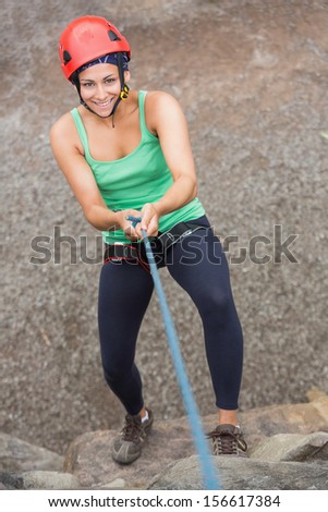Smiling girl abseiling down rock face looking up at camera