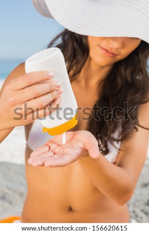 Sexy young brunette on the beach protecting her body with sun cream
