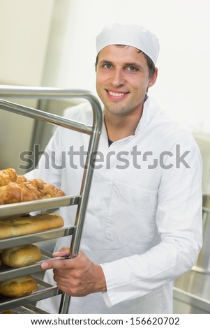 Young baker pushing a trolley with food on it while smiling at the camera