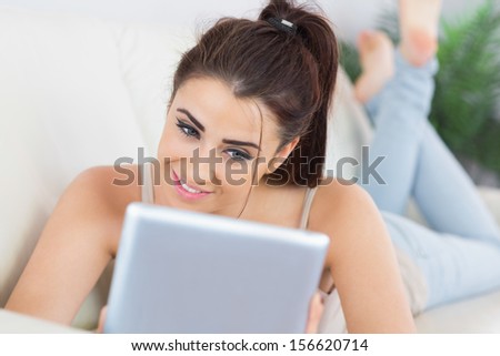 Pretty casual woman using her tablet lying on a couch in the living room